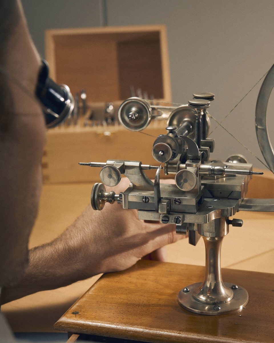 A complex, metallic watchmaking instrument on a stand