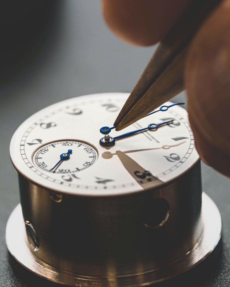 Watchmaker using tweezers to place hands on a watch dial.