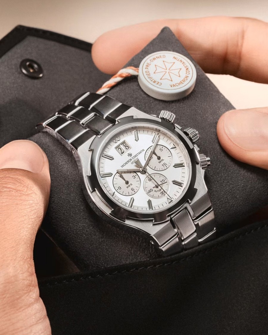 A silver metal watch sits in a dark open box held by hands