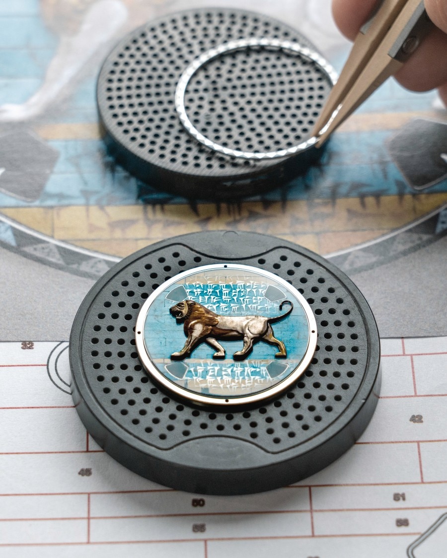 Hand assembling a watch dial featuring an enamel lion design.