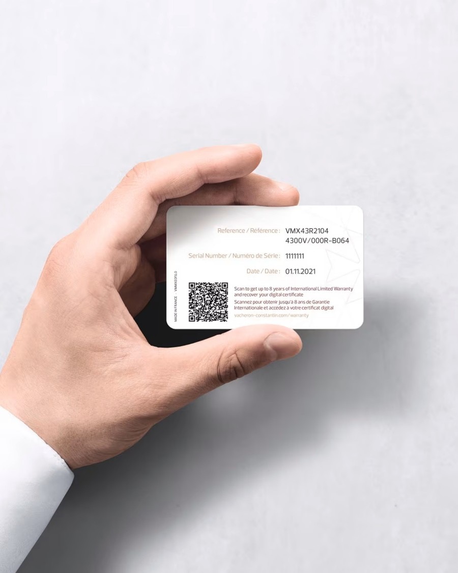 A hand holding a Vacheron Constantin white warranty card with a QR code and typed details about the watch