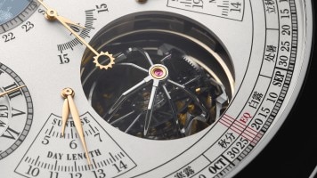 Close-up of a watch dial showing calendar scales and a visible tourbillon.