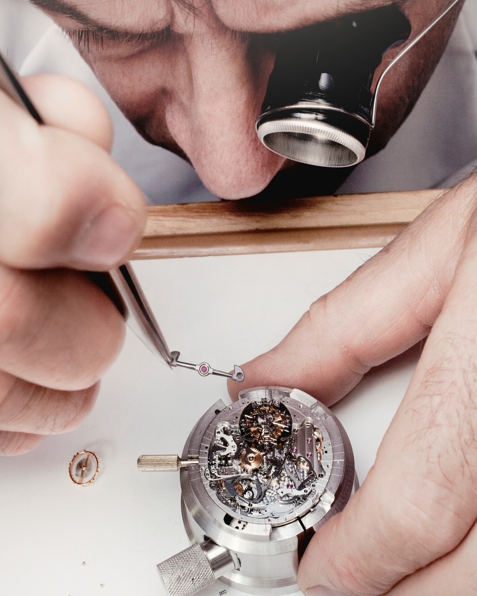 Watchmaker using tweezers to place a part into a mechanical movement.
