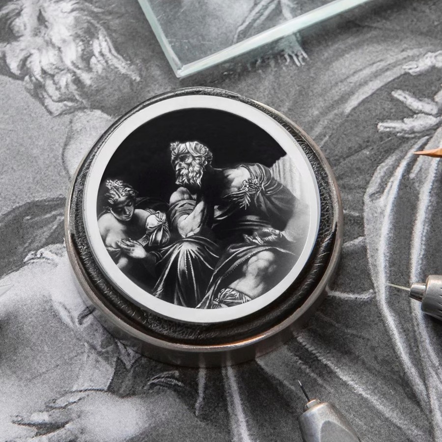 A detailed engraving on a circular metal object depicts a bearded man seated and a woman beside him.