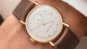 A man's wrist with a classy watch with golden details and a leather strap.