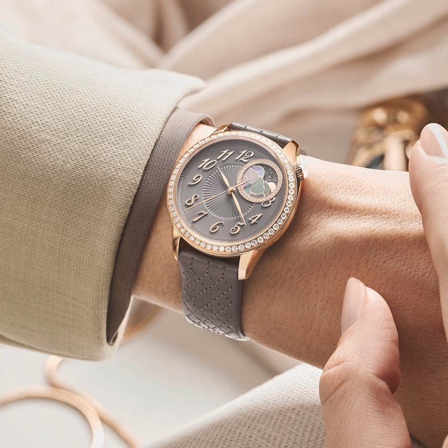 Close-up of a woman's hand in a light suit wearing a watch with a grayish leather strap and a gold frame