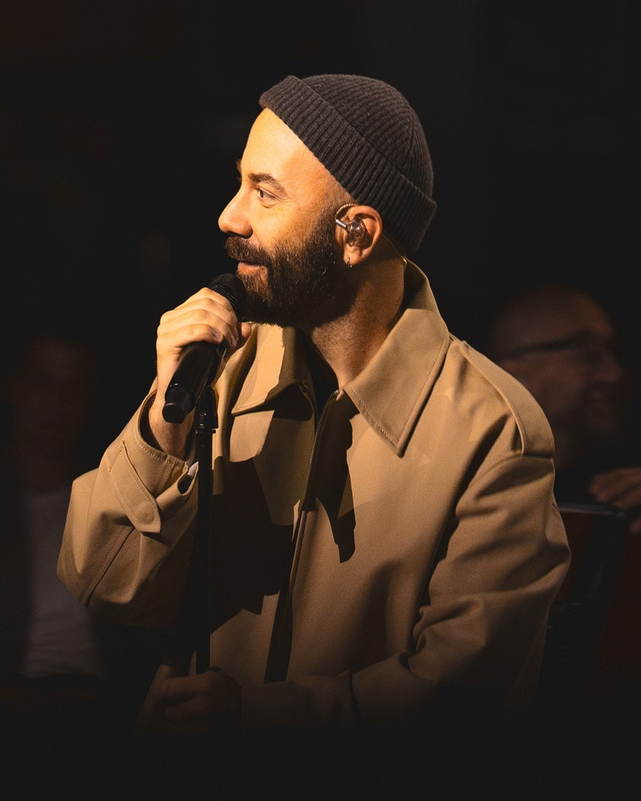 A man in a beige coat and black beanie holding a microphone