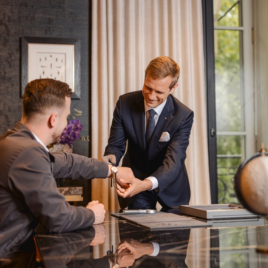 Boutique consultant helping a client try on a watch in a luxury store setting.