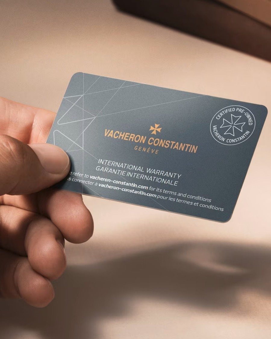 A hand holds a dark rectangular Vacheron Constantin international warranty card.
