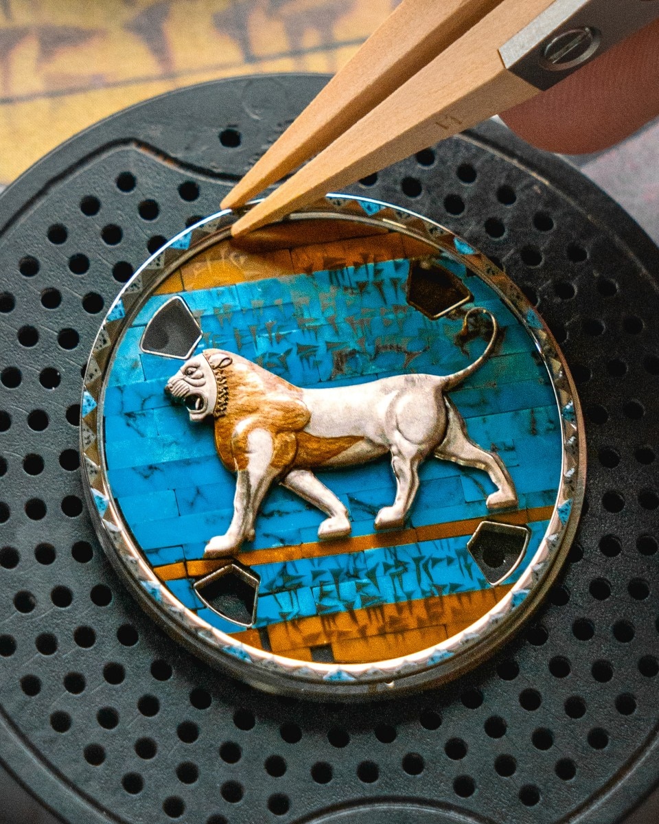 Tweezers placing an enamel dial with a lion design onto a watchmaking holder.