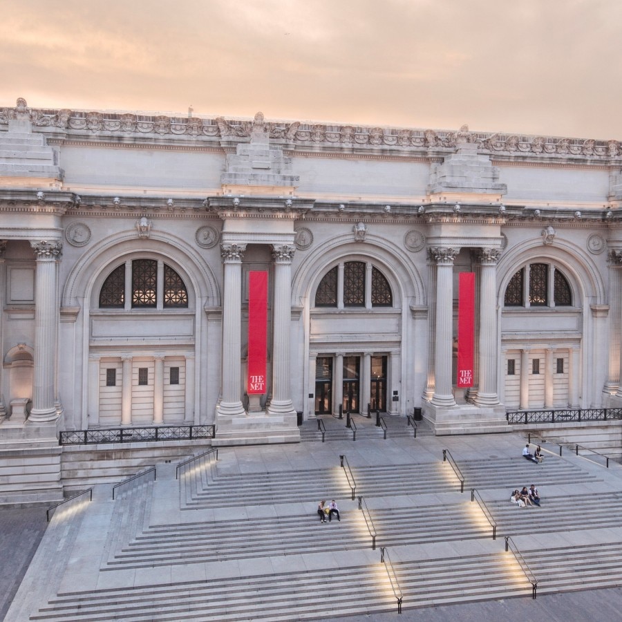Exterion view of the Met museum with wide steps and red banners.