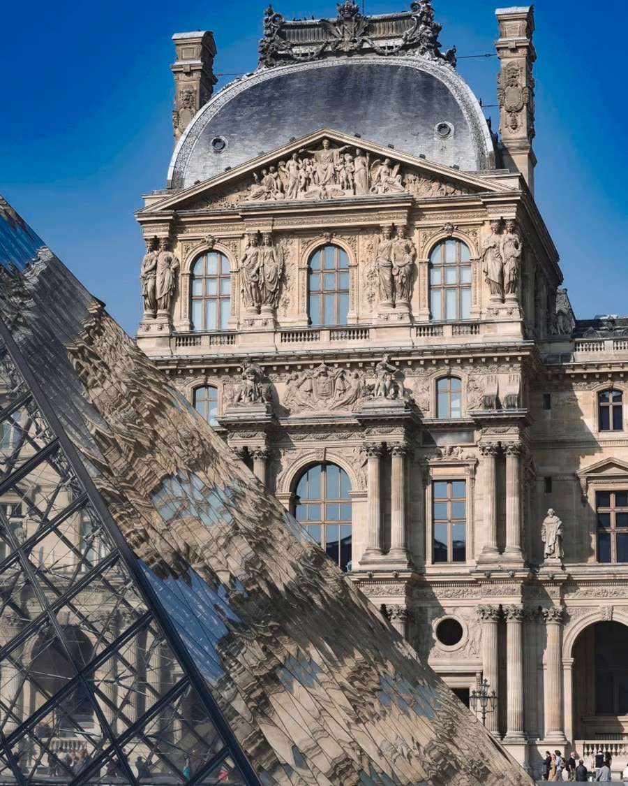 Historic Louvre building in Paris with a glass pyramid in the foreground.