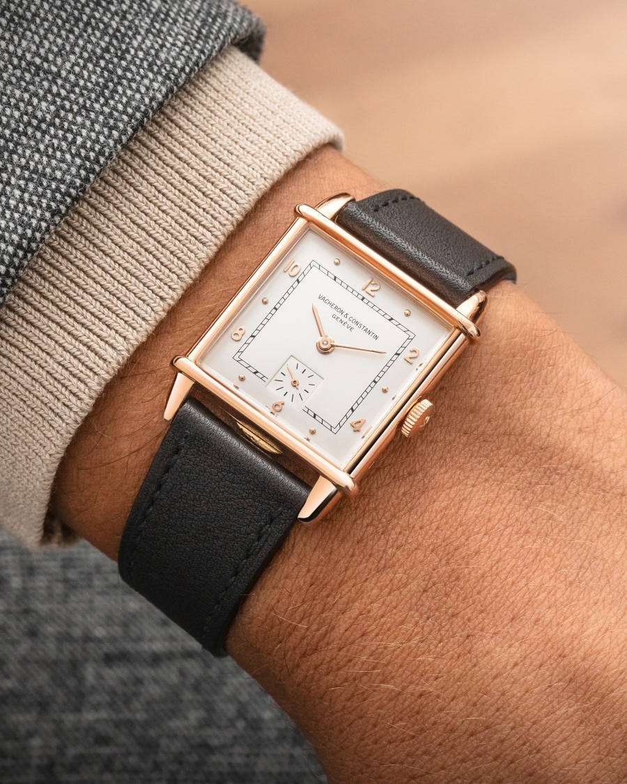 A watch with squared case and a dark leather strap.
