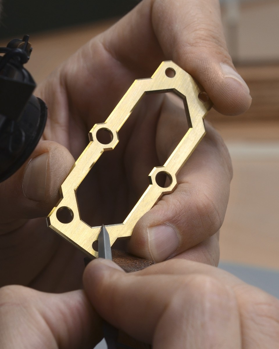 Hand finishing the edges of a gold watch component.