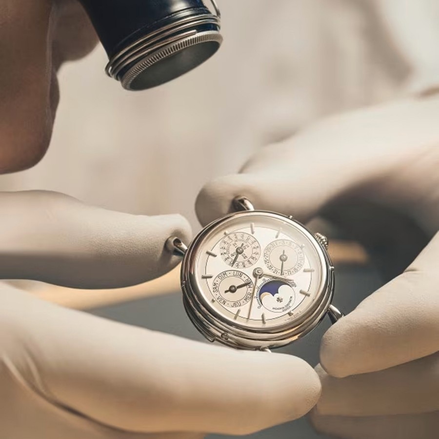 A watchmaker checks a watch under a magnifying glass.